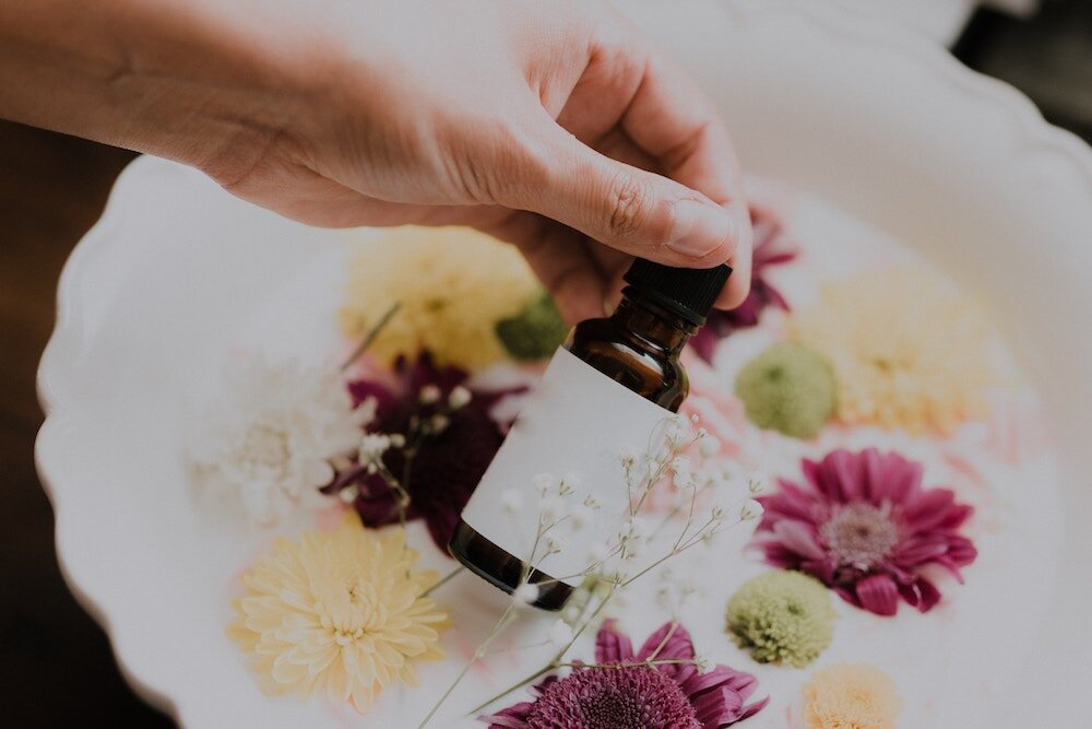 hand holding essential oils bottle with flowers in the background representing a natural morning sickness remedy