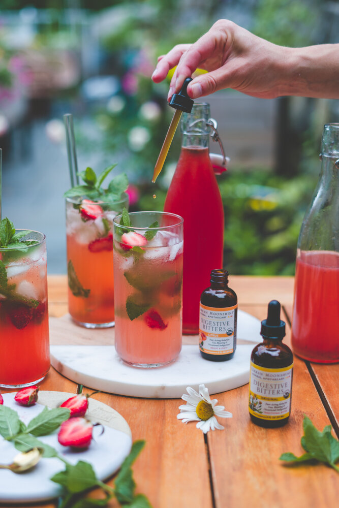 how to make a strawberry shrub recipe featured on a table with a garden