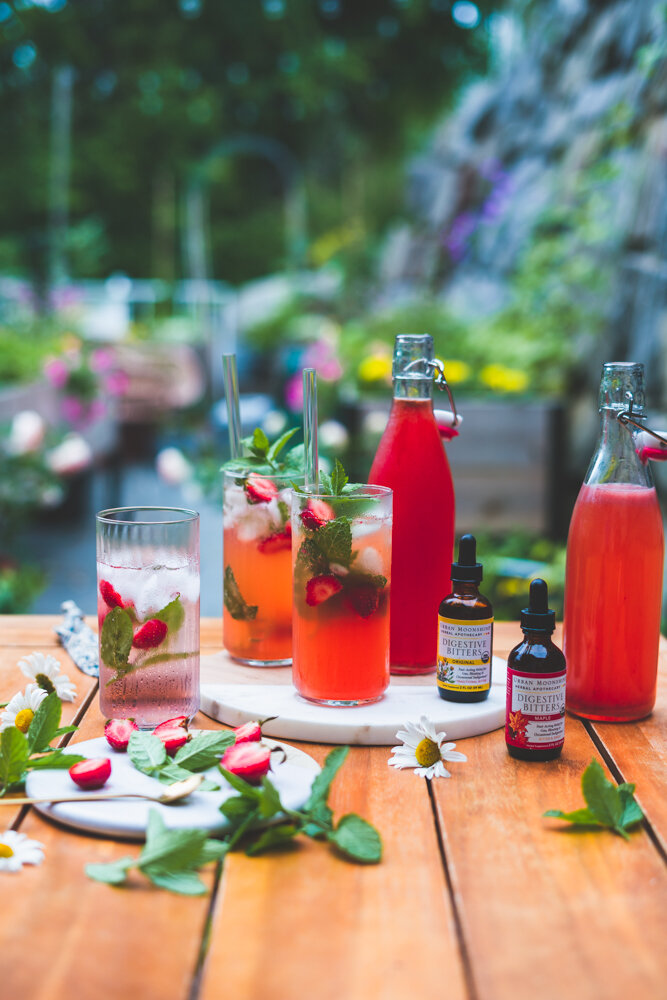 how to make a strawberry shrub recipe featured on a table with a garden