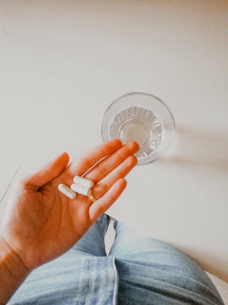 woman holding vitamins over water when to start taking prenatal vitamins