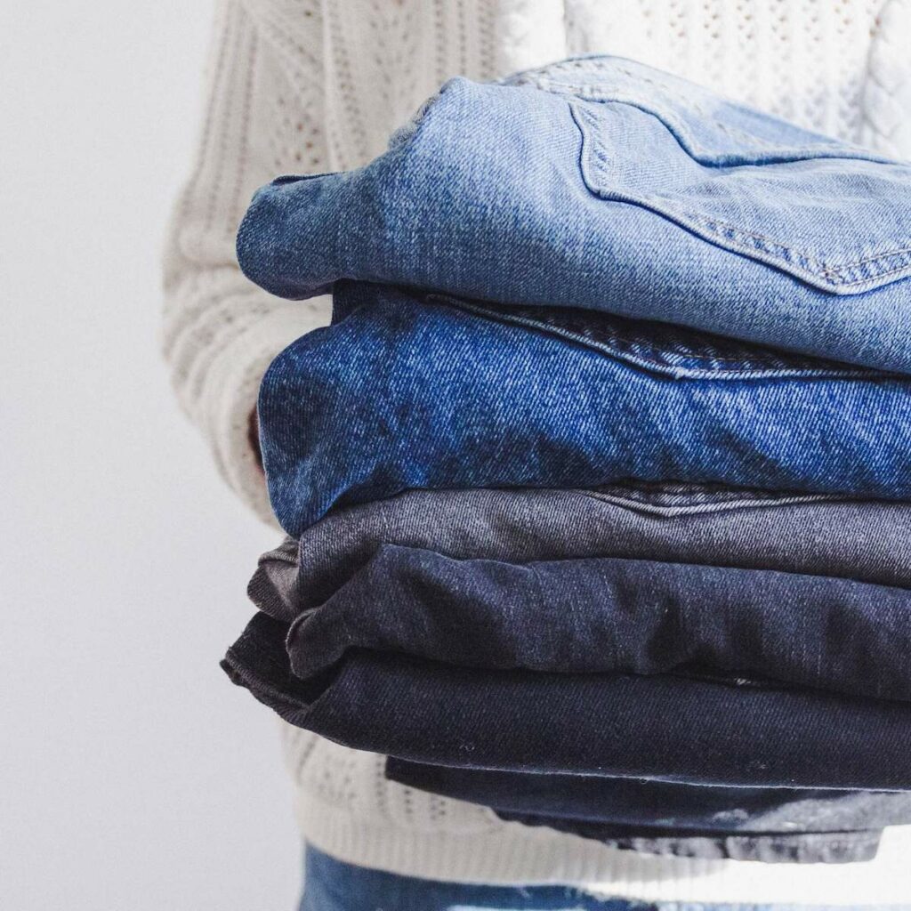 a woman holding a stack of denim jeans