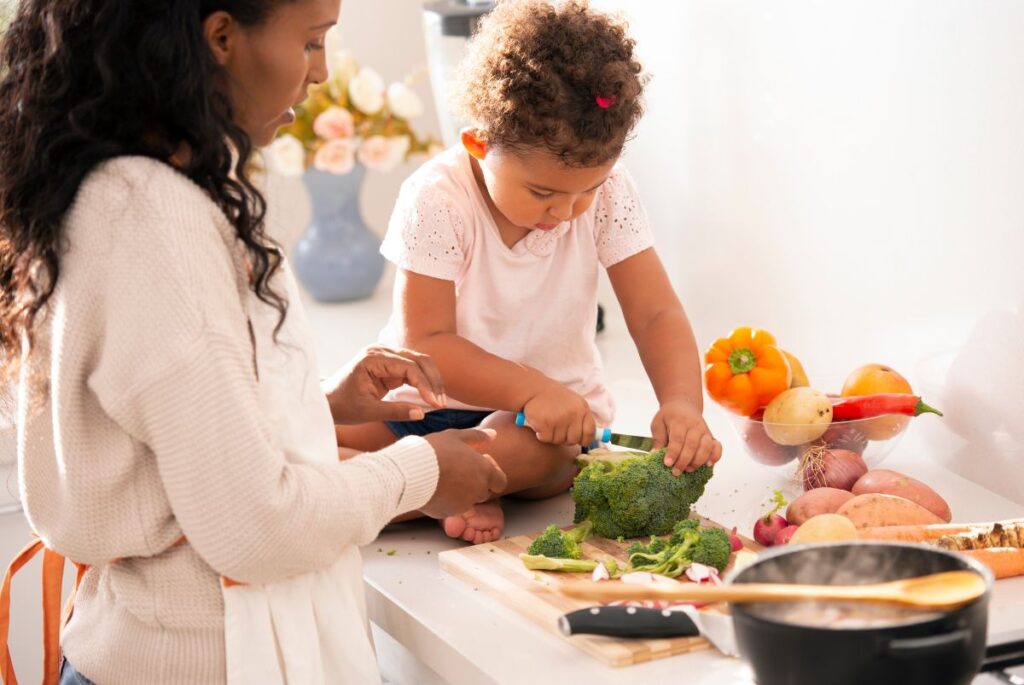 child cutting vegetables with her mother on the counter